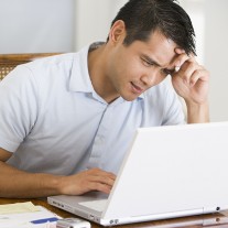 Man in dining room using laptop and frowning